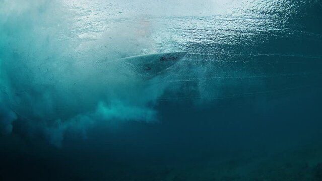 Surfer underwater. Man dives under the wave with surfboard to pass the wave. Underwater view of the surfer duck diving under the wave