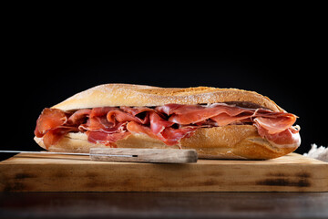 Spanish serrano ham sandwich on wooden table and black background