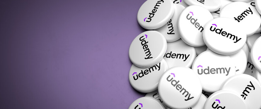 Logos of Udemy the online learning and teaching platform and company on a heap on a table. Copy space. Web banner format.