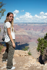 Naklejka premium Vertical photography of a young blonde girl with a photo camera in front of the landscape of the Grand Canyon