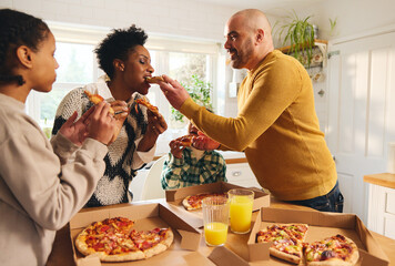 Family eating takeaway pizza at home, man feeding woman