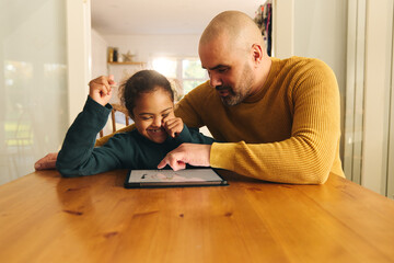 Multiracial father and son with Down syndrome using digital tablet for homework