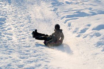 Fototapeta na wymiar The boy rolls down the mountain on a tubing in winter