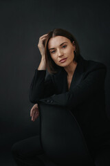 Naklejka premium Portrait of a modern stylish woman. Beautiful brunette woman posing on a chair on a black background.
