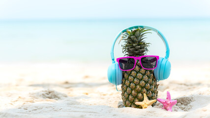 Summer in the party.  Hipster Pineapple Fashion in sunglass and listen music with sunblock and sandal on the sand beach beautiful blue sky background.  Fashion Summer Vacation Concept