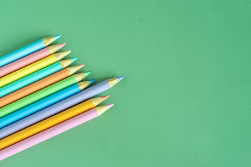Pastel colored pencils, top view on green background, illustration concept, education and back to school