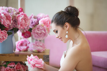 Gentle portrait of a beautiful woman in a bright interior among pink peonies.