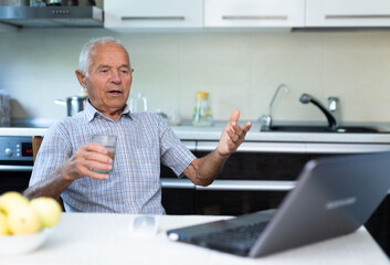 Naklejka na ściany i meble Elderly man with glass of wine communicates virtually using a laptop and the Internet