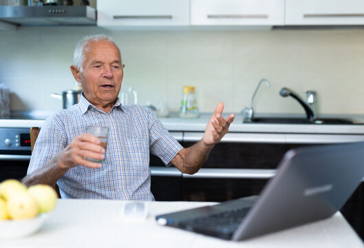 Elderly Man With Glass Of Wine Communicates Virtually Using A Laptop And The Internet