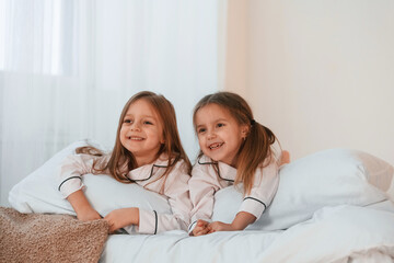 Lying down on the bed. Two little girls are playing and having fun together in domestic room