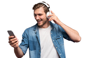 Excited young man wearing jeans shirt standing isolated over transparent background, listening to music with earphones and mobile phone