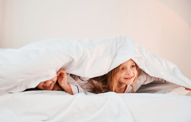 Fototapeta premium Kids are lying down on the bed. Two little girls are playing and having fun together in domestic room