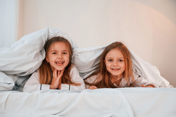 Kids are lying down on the bed. Two little girls are playing and having fun together in domestic room