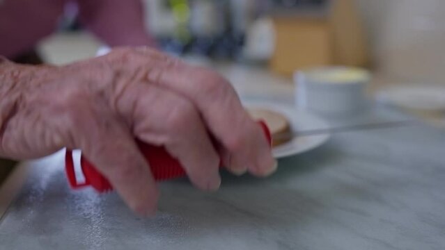 Close Up Of Senior Man With Arthritis In Kitchen Using Adapted Cutlery To Butter Bread