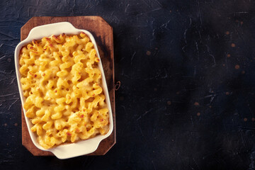 Macaroni and cheese pasta in a casserole dish, shot from the top on a black background with a place...