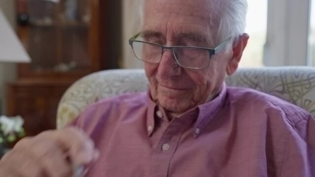 Senior Man Sitting In Armchair At Home Enjoying Sudoku Puzzle Book