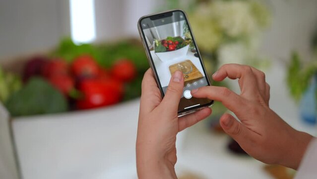 Close-up smartphone screen with female hand taking photo of home-grown vegetable basket. Unrecognizable Caucasian young woman photographing tasty ripe veggies with phone app
