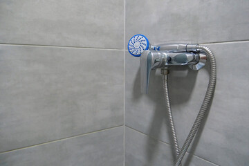 Shower head in bathroom, chrome faucet and grey tiles on walls