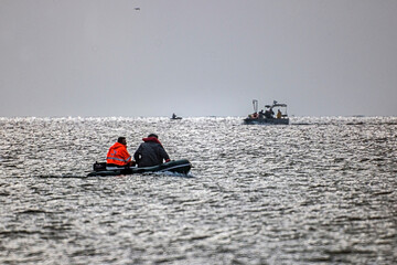 Two fishermen on a motor boat in the sea against the background of another small boat	
