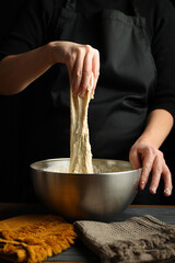 The cook kneads the dough on a black background in a bowl.