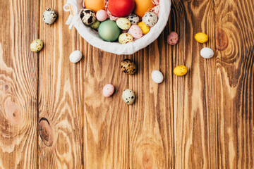 Colored eggs of different sizes in a straw basket on a wooden background. Symbol of the Easter holiday. Easter background. Top view