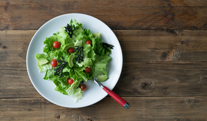 White plate of mixed salad with seaweed, tomatoes, lettuce and avocado. Wood background. Copy space.