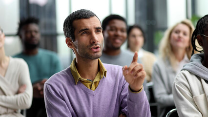 He got some questions. Group of young people sitting on conference together while one man raising...