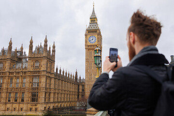 Man takes a photo of Big Ben and Westminster palace on smartphone in London, traveling and tourism,...