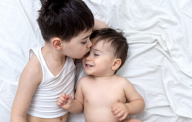 Obraz na płótnie Canvas emotional photo with two brothers lying on bed hugging kiss each other cuddling and caresses.big brother kissing little one.different face expression emotion kids child baby boy maternity concept top 