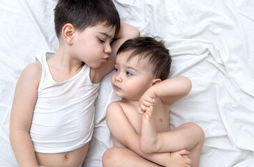 Fototapeta na wymiar emotional photo with two brothers lying on bed hugging kiss each other cuddling and caresses.big brother kissing little one.different face expression emotion kids child baby boy maternity concept top 