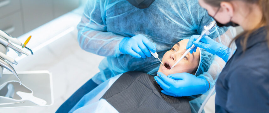Male dentist and assistant with female patient in dental chair providing oral cavity treatment.