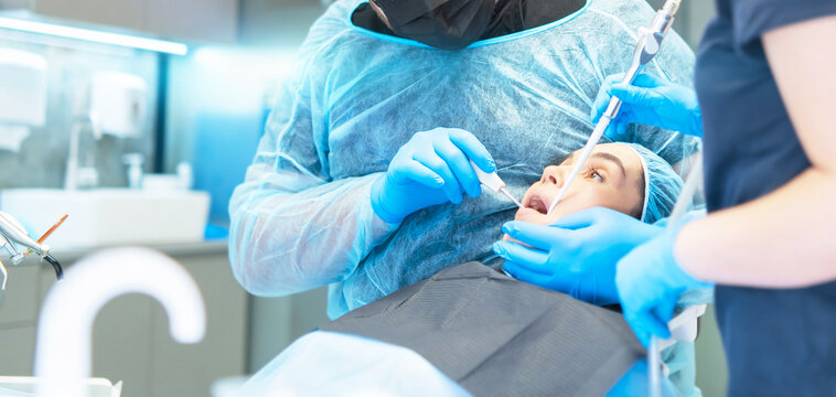 Male dentist and assistant with female patient in dental chair providing oral cavity treatment.