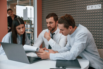 Sitting, talking, using laptop. Office workers are indoors by the table