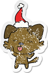 distressed sticker cartoon of a dog sticking out tongue wearing santa hat