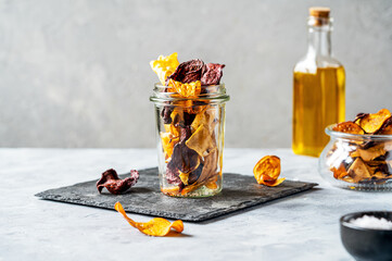 Healthy vegetable chips in a glass jar on stone cutting board with marine salt and oil aside....