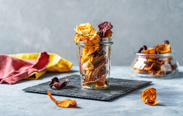 Healthy vegetable chips in a glass jar on stone cutting board. Concrete background