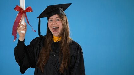 Graduate girl with diploma, shows gesture of victory and success on blue background, celebrating graduation from the high school or University, excited dancing party