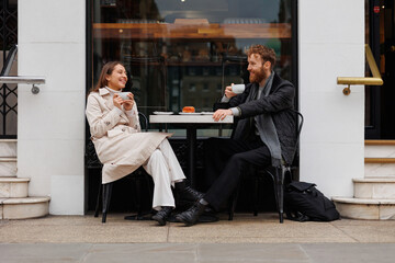 Happy couple drinking coffee and laughing talking to each other sitting at the table of outdoor...