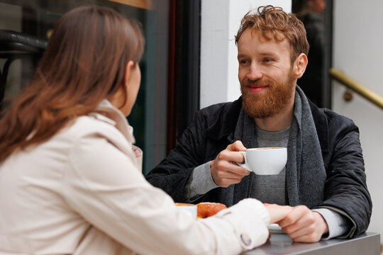 Happy couple drinking coffee and laughing talking to each other sitting at the table of outdoor cafe on city streets