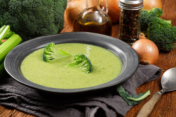 Creamy broccoli soup in a black plate on a wooden background