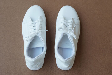 Pair of new white shoes, sneakers isolated on brown background. Concept, unisex footwears fashion. Daily life wearing for traveling, doing sport. Go with comfortable shoes.             