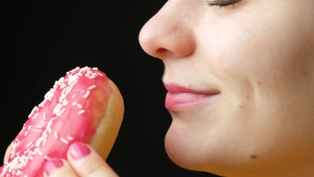 A woman is going to eat a donut, sniffs it and licks it. The smell and taste of food, delicacies, a lot of calories.