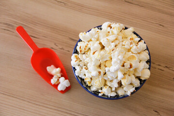 Fried white airy popcorn in a decorative plate and in a red spoon on a brown wooden background