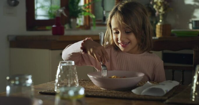 Portrait of a Cute Little Girl Eating Delicious Pasta for Lunch and Thanking her Mother for Cooking it. Happy Female Child Enjoying her Home-Cooked Meal While Sitting in the Kitchen