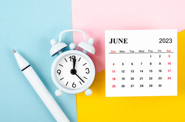 The June 2023 Monthly calendar with alarm clock and pen on beautiful background.