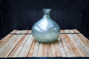 Ein Stillleben mit einer Blauen Vase auf einem Stapel Holzlatten, vor einem dunklen Hintergrund.
