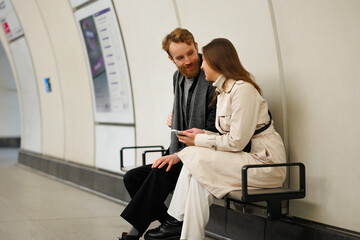 Happy couple is sitting on a subway station bench and talking