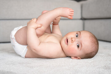 childhood, babyhood and people concept - happy little baby boy or girl lying on floor at home