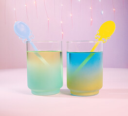 A Pastel Spring Cocktail Duo: Two Colorful Pastel Blue and Green Beverages with Ornate, Victorian Style Swizzle Stick with Fairy Lights and Pink Background