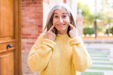 senior retired pretty white hair woman smiling confidently pointing to own fake smile